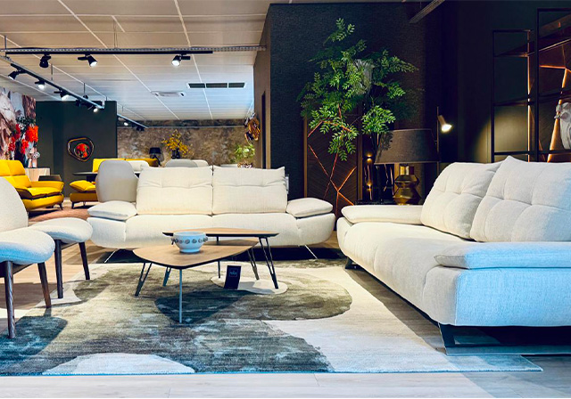 Salon spacieux avec deux grands canapés clairs, tables basses en bois, tapis graphique et décor chaleureux avec éclairage tamisé.