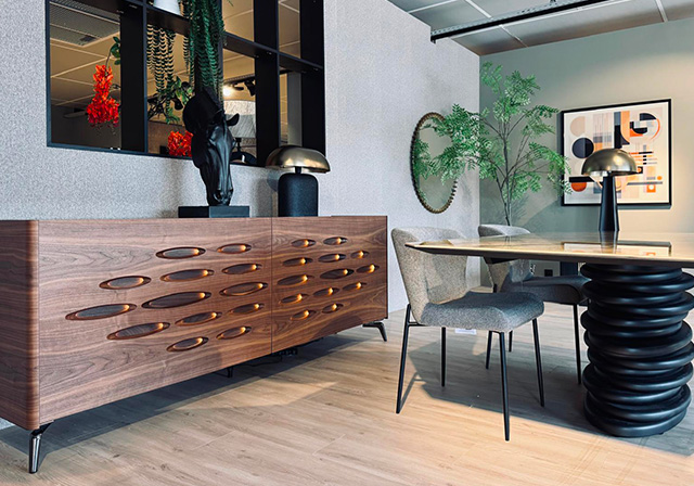 Salle à manger au design audacieux avec table ronde pied sculptural noir, chaises grises et buffet en bois sculpté avec éclairage intégré.
